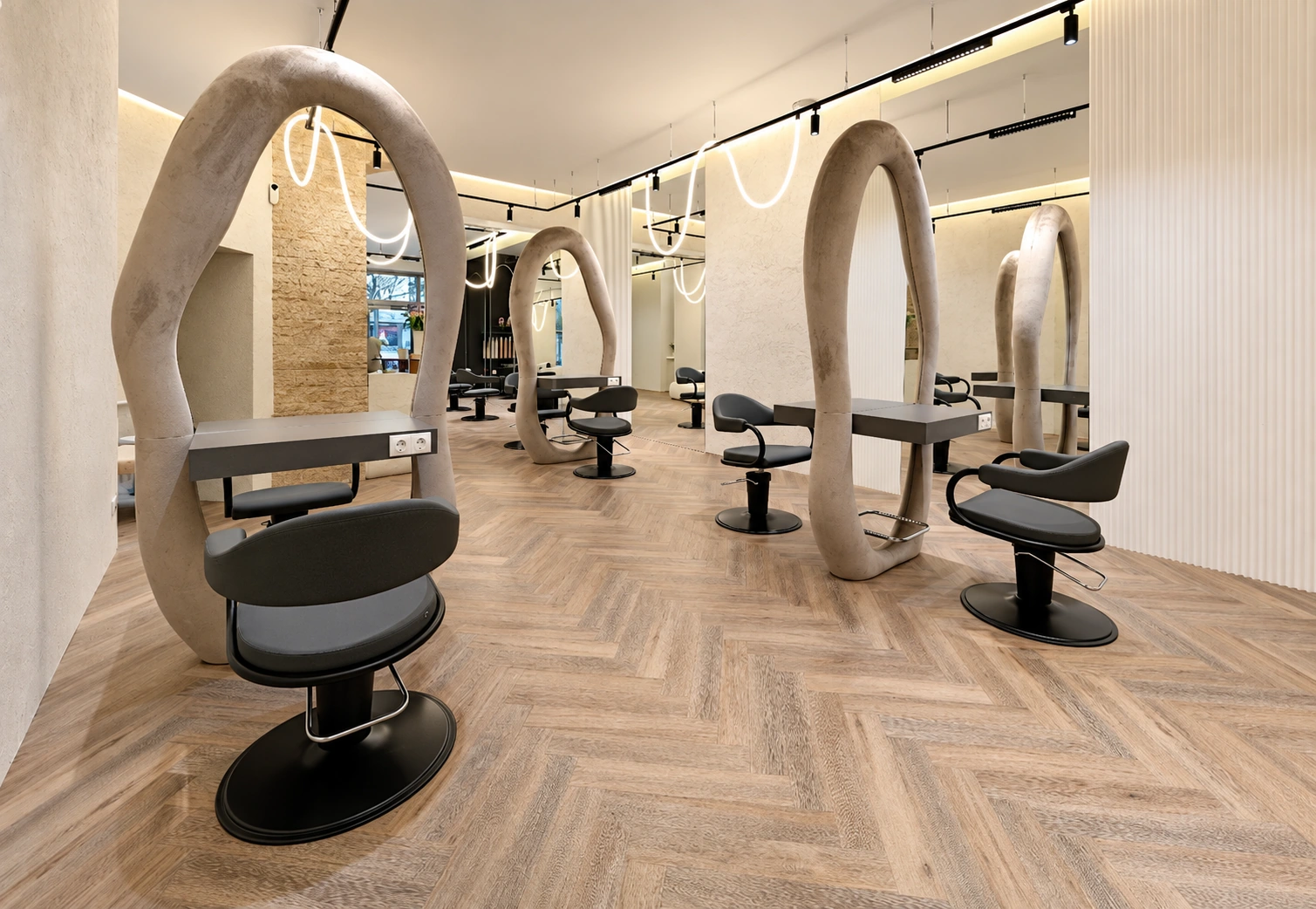 Offener Salon mit skulpturalen ovalen Spiegeln, dunklen Stylingstühlen und Fischgrätboden